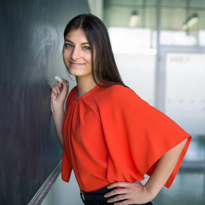 Smiling teacher writing in a notebook in a classroom with a chalkboard full of math equations