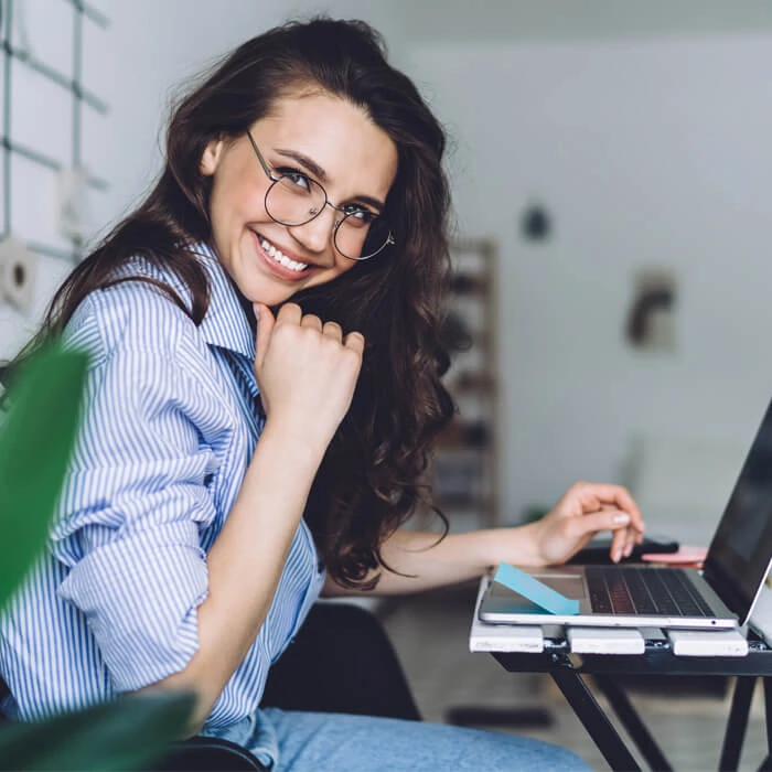 Smiling young woman in library reading a book while sitting at a desk
