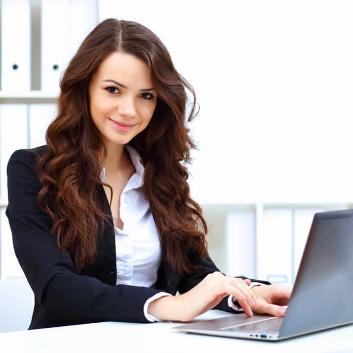 Confident female student smiling while working on laptop in modern office setting